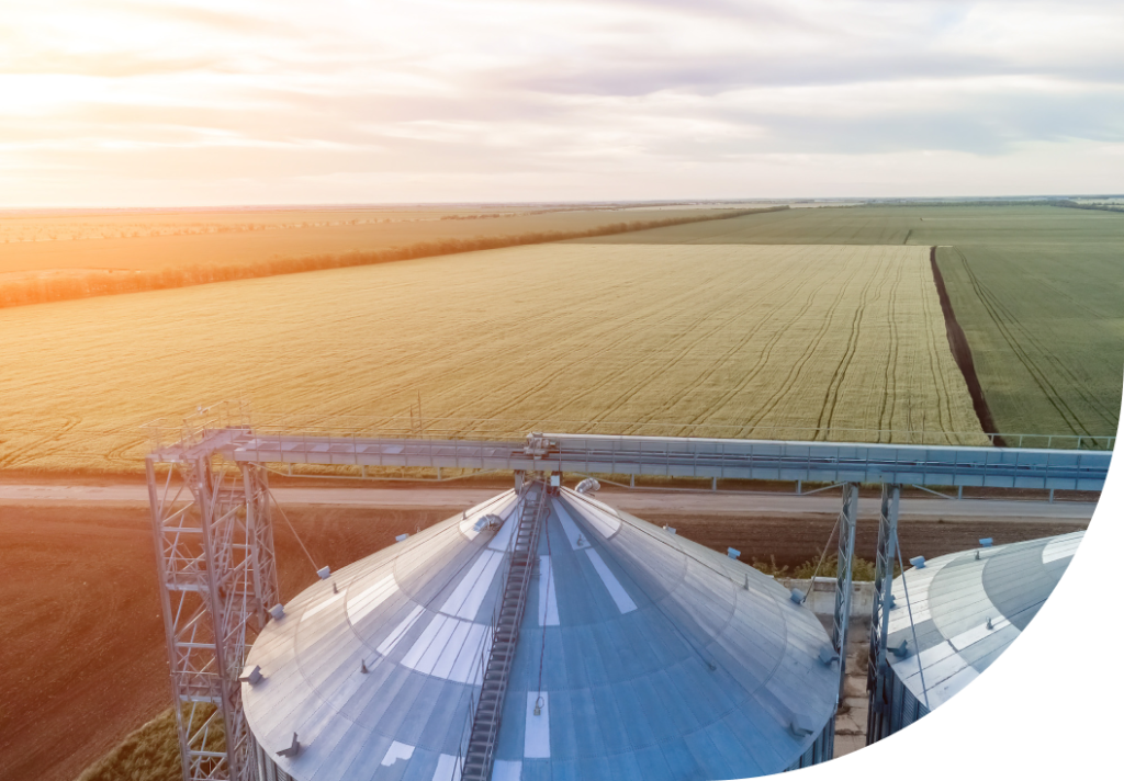 A wide shot of feed silos overlooking vast farm fields at dusk.